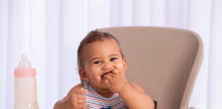 Cute baby child eating food, sitting on high chair.