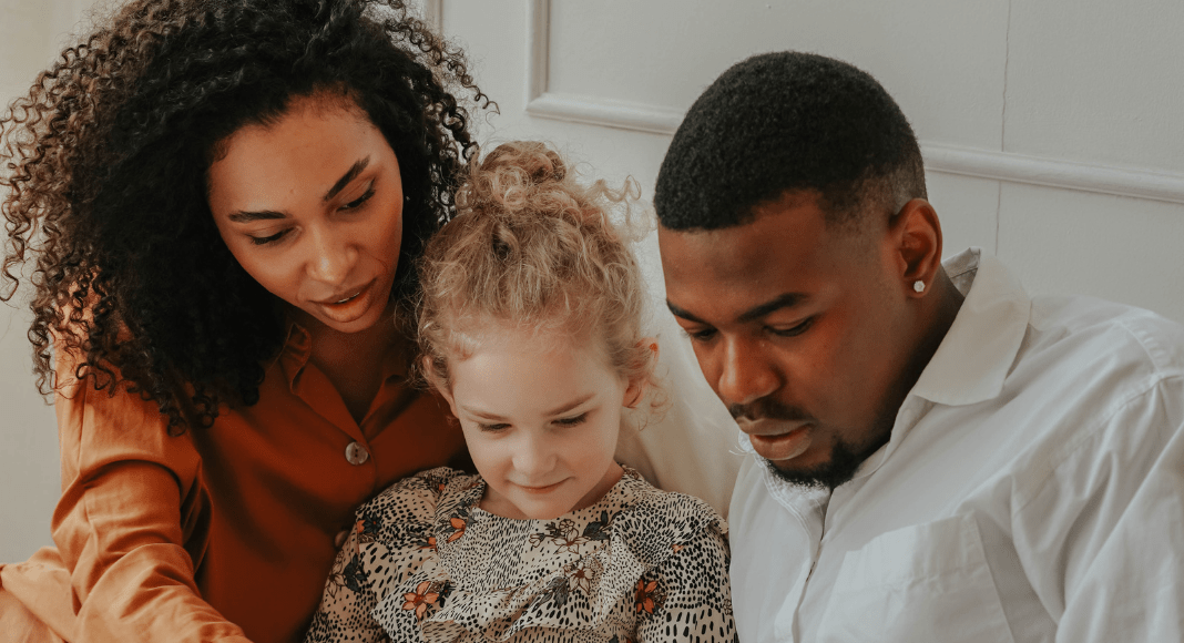 Two parents read a book with their child.